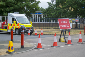 Line Of Traffic Cones Blocking Road Junction, With Traffic Management Vehicle Behind The Cones.