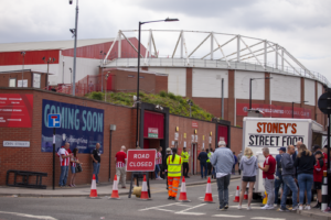 A Line of Traffic Cones Is Spanning A Junction Along With A Sign That Reads "ROAD CLOSED". Bramall Lane Stadium is in the background.
